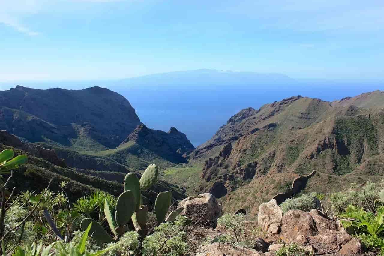 A view of a valley with mountains and a body of water in the background.