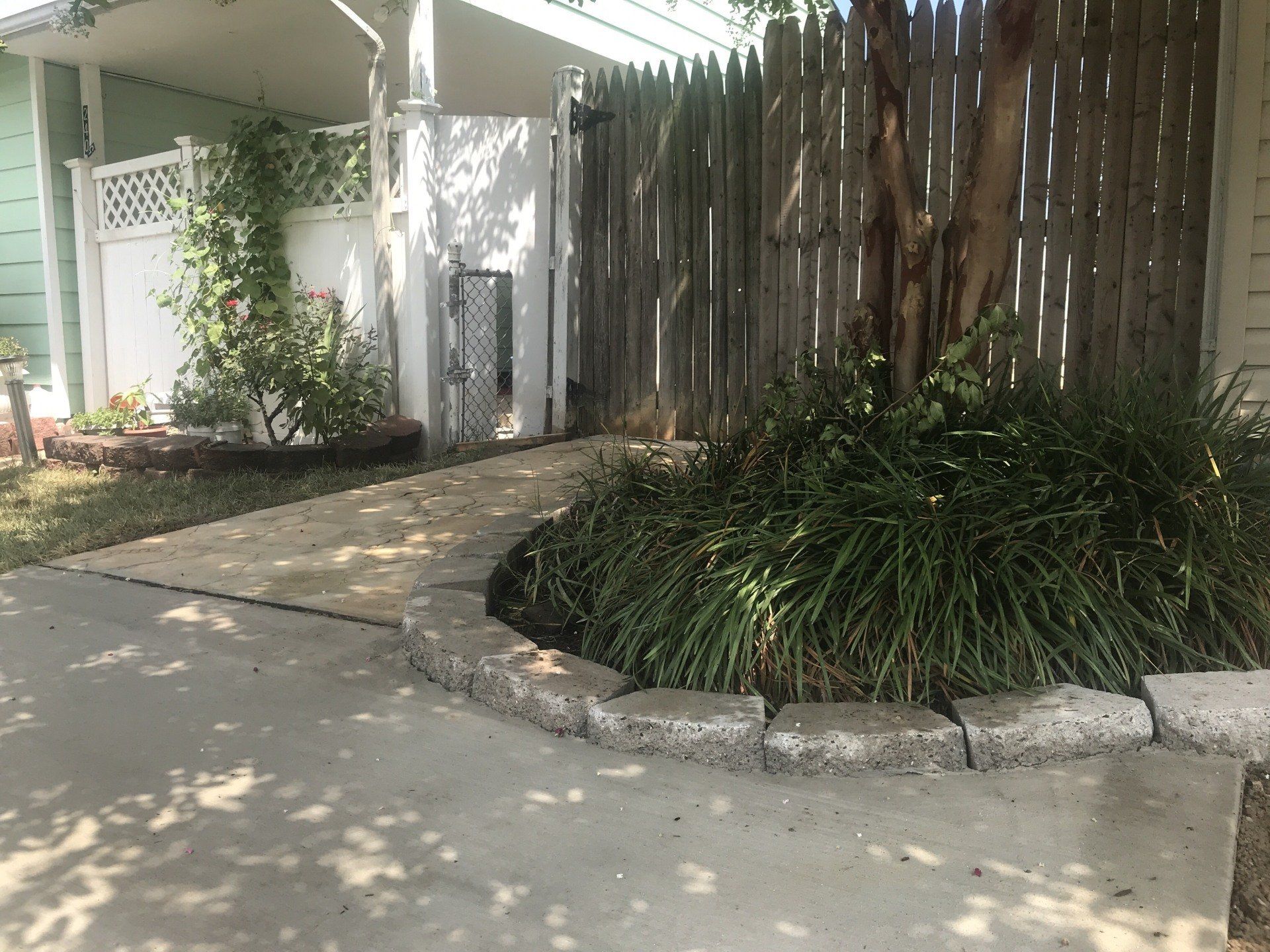 Pathway bordered by stone leads to gate, surrounded by a wooden fence, with lush greenery.