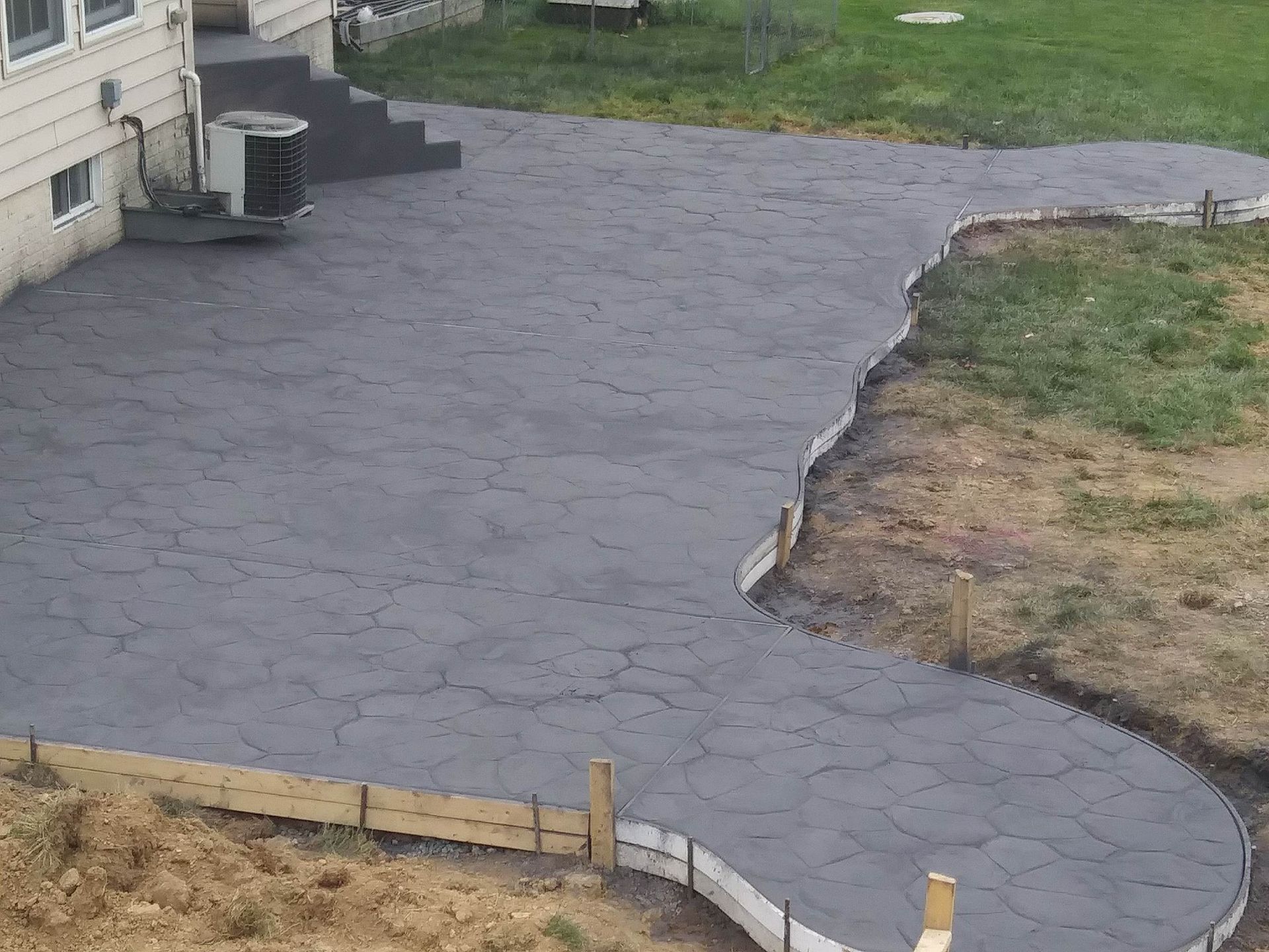 Gray concrete patio with stairs next to a house and grassy area with a wooden border.