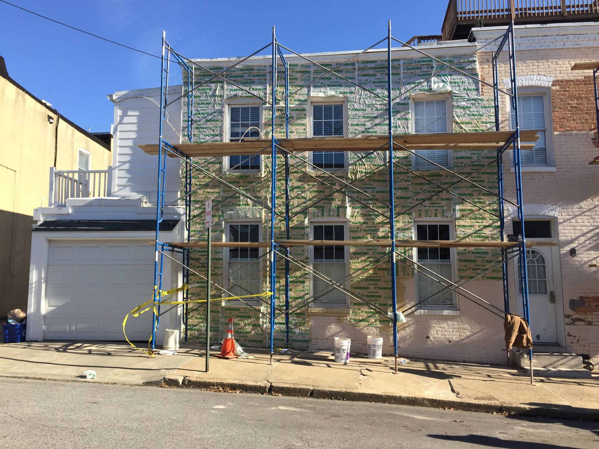 Building facade under construction, scaffolding erected. The front of a house, painted blue and green, with workers present.