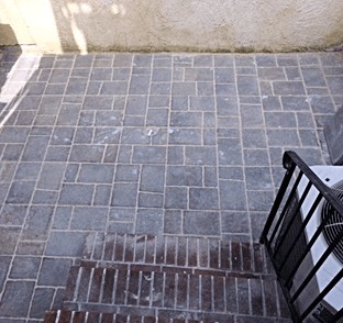 Gray brick patio with irregular pattern, steps with brick border, black railing, light-colored wall.