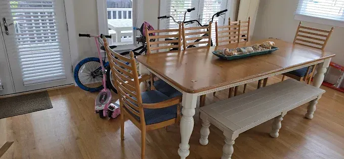 Dining room with a table and chairs. A bench sits on one side. Scooters and bikes are present.