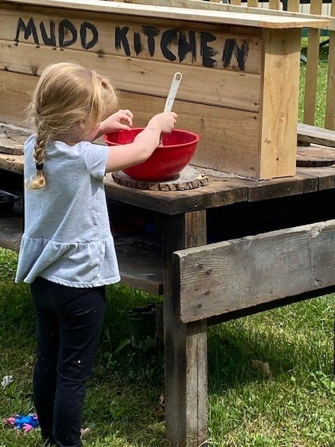 Girl stirring a red bowl with a spoon at a wooden 