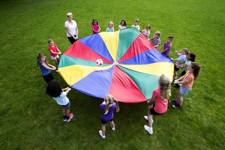 Children playing with a colorful parachute on a grassy field, a ball in the center.