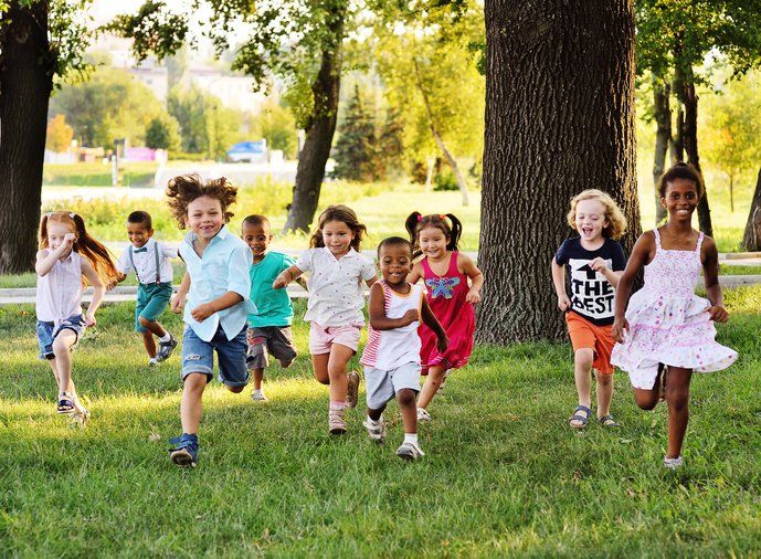 Children running and playing on green grass near trees in a park.