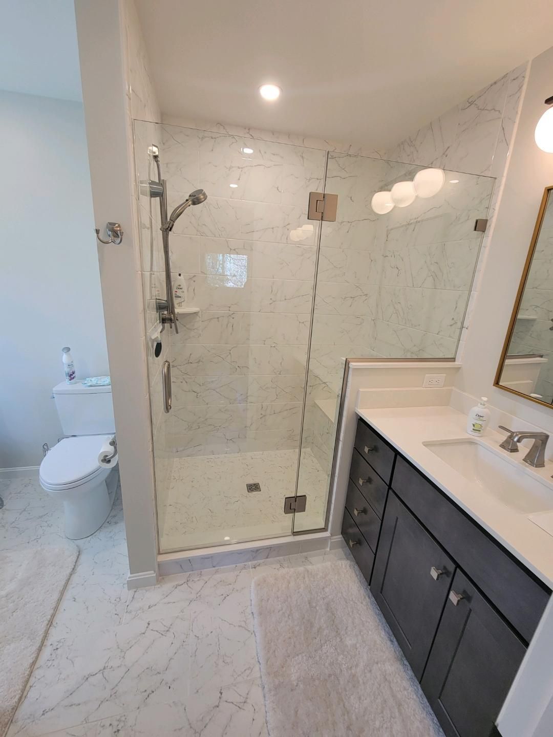 Modern bathroom with a glass-enclosed shower, vanity, and toilet. White marble floors and walls, gray cabinet.