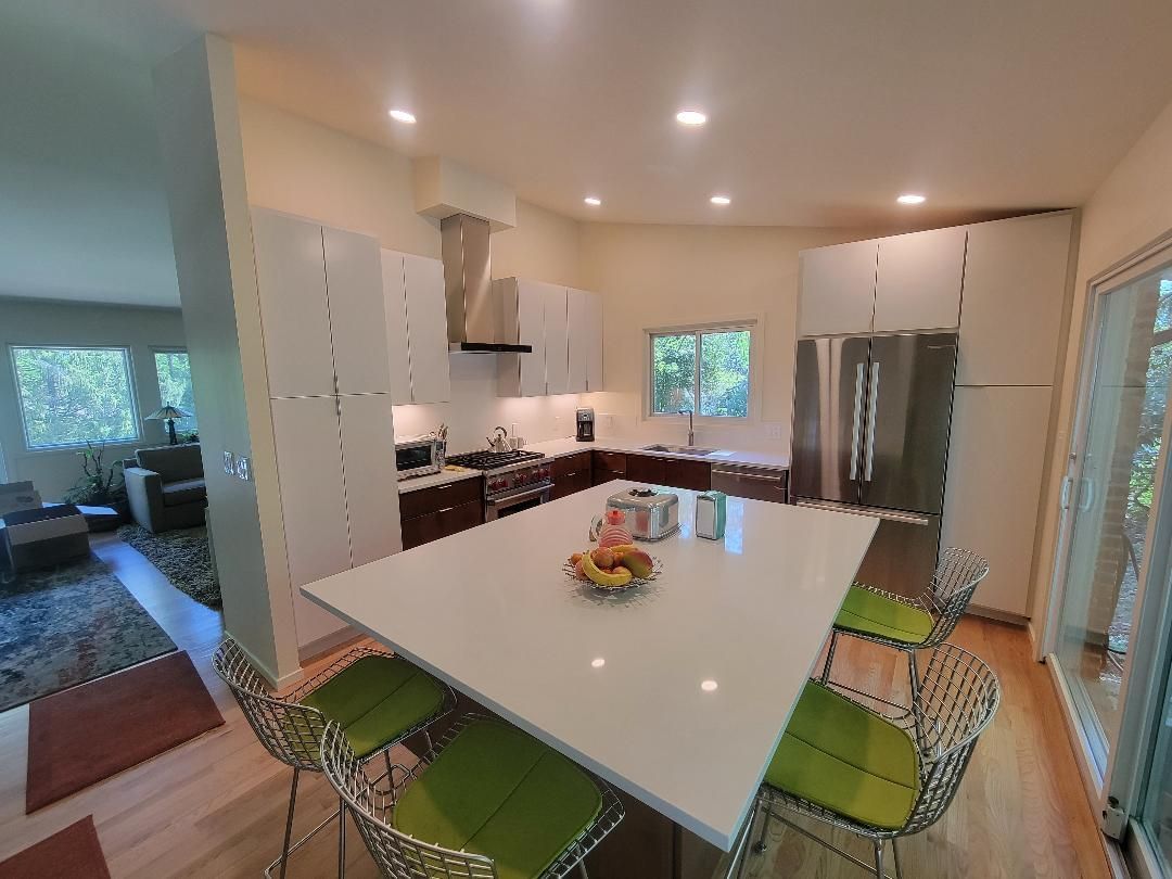 Modern kitchen with white cabinets, large island, stainless steel appliances, and green bar stools.