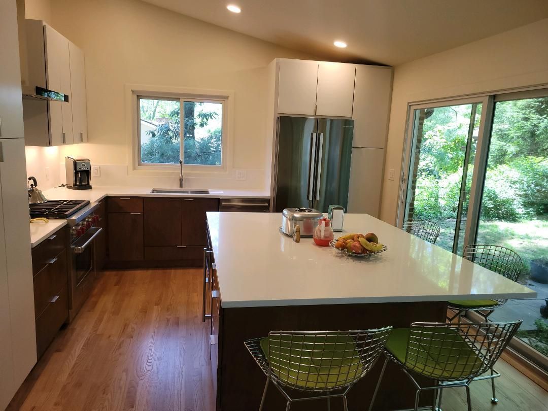 Modern kitchen with island, dark cabinets, white countertops, stainless steel appliances, and a sliding glass door to the outdoors.