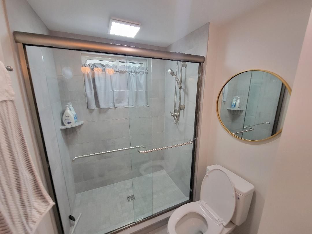 Bathroom with glass shower, toilet, round mirror, and towel rack.
