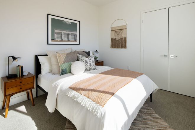 A bedroom with a bed , nightstand , lamp and picture on the wall.