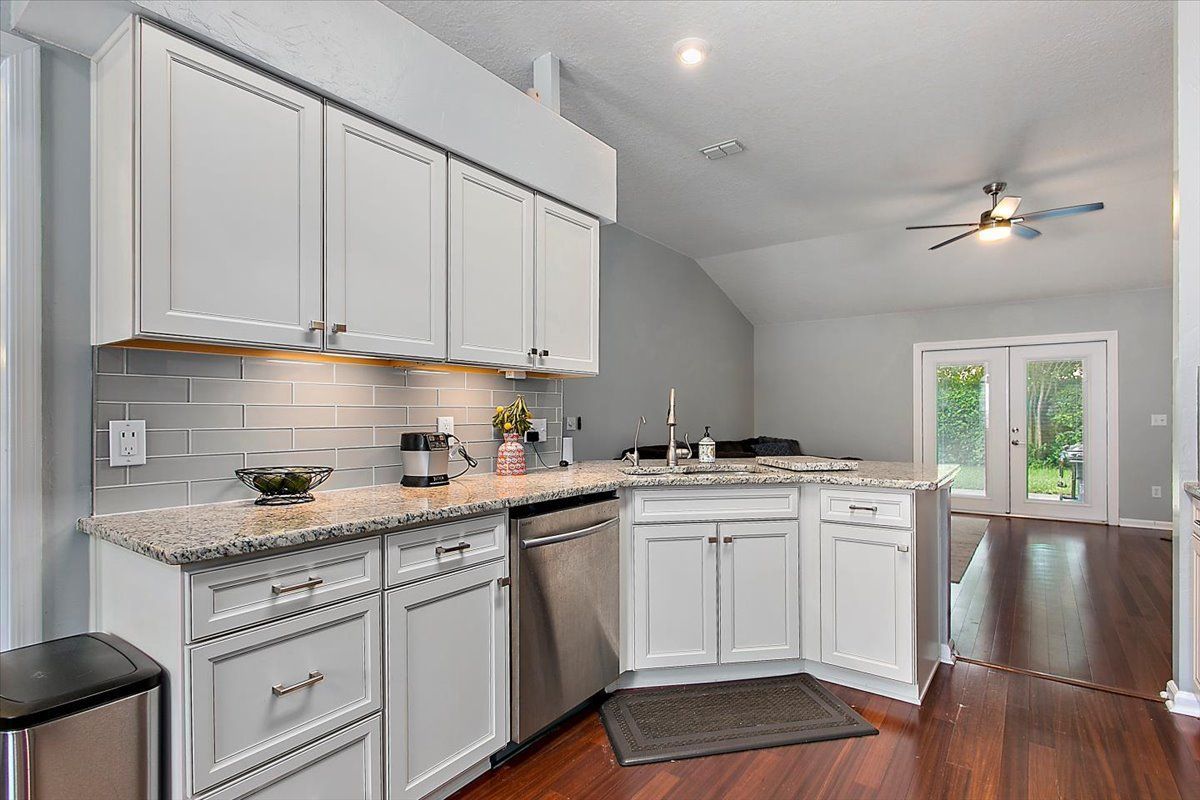 Modern kitchen with white cabinets, stainless appliances, dark wood floors, and French doors to a bright dining area