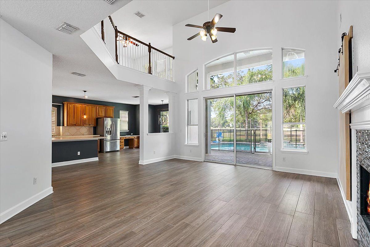 Spacious modern living room with vaulted ceiling, hardwood floors, fireplace, and large windows overlooking a patio