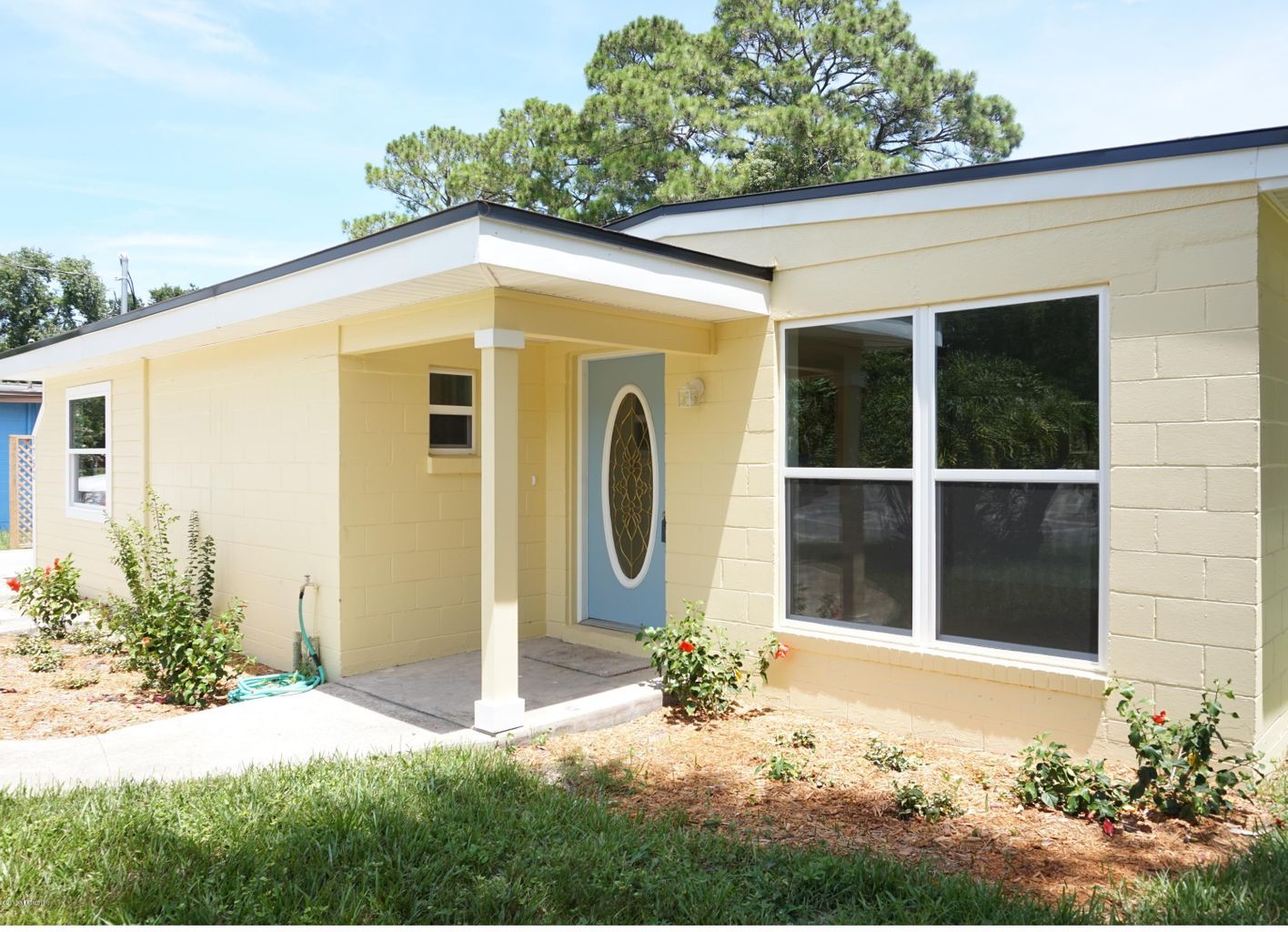 Single-story cream house exterior with a front porch, oval glass door, and large windows