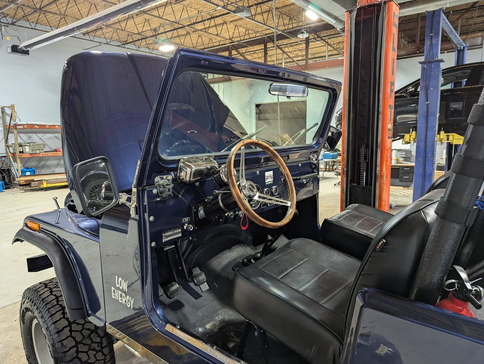 Dark blue Jeep interior with a wooden steering wheel and black seats.