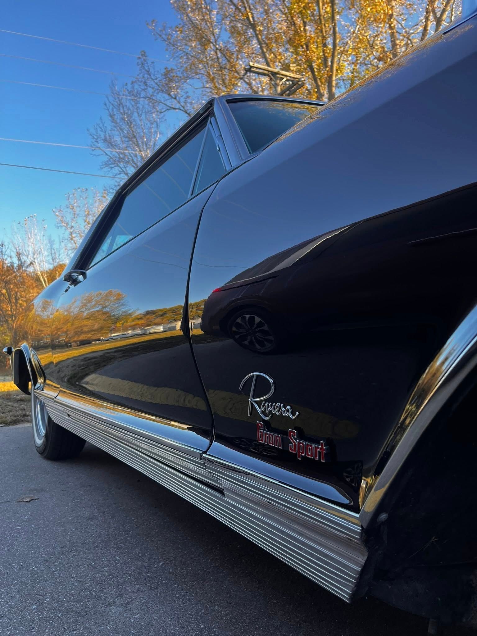 Black vintage Buick Riviera with chrome trim, parked outdoors on a sunny day.