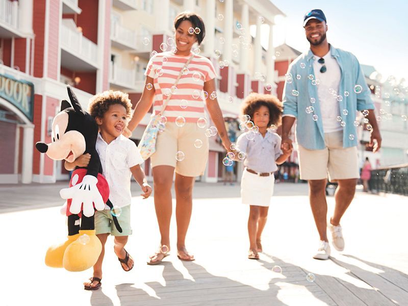 A family is walking down a sidewalk with a mickey mouse stuffed animal.