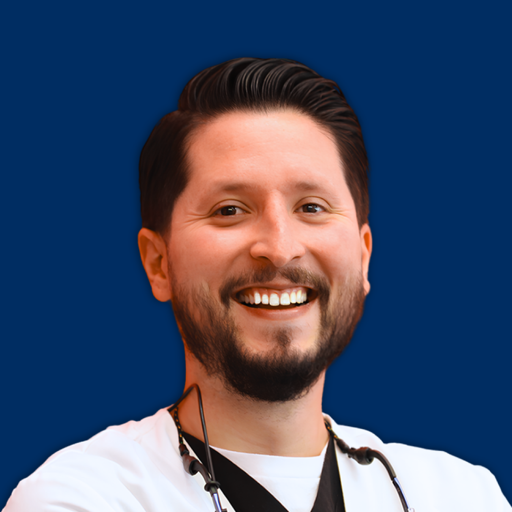 Smiling person with dark hair and beard against a solid blue background, wearing a white shirt and stethoscope
