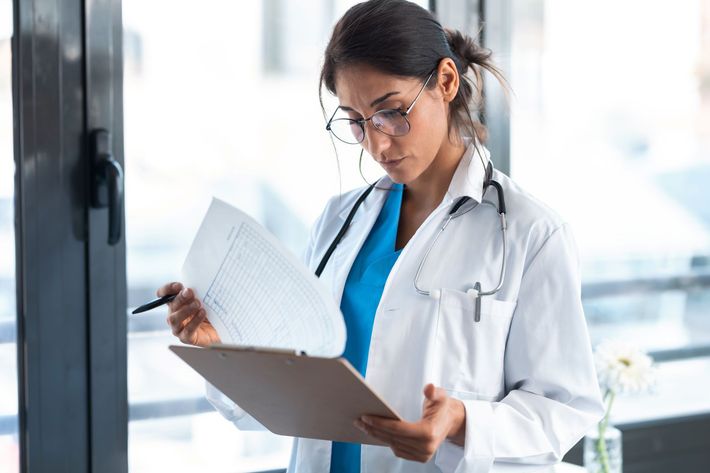Doctor in white coat reviewing a clipboard in a bright clinic hallway