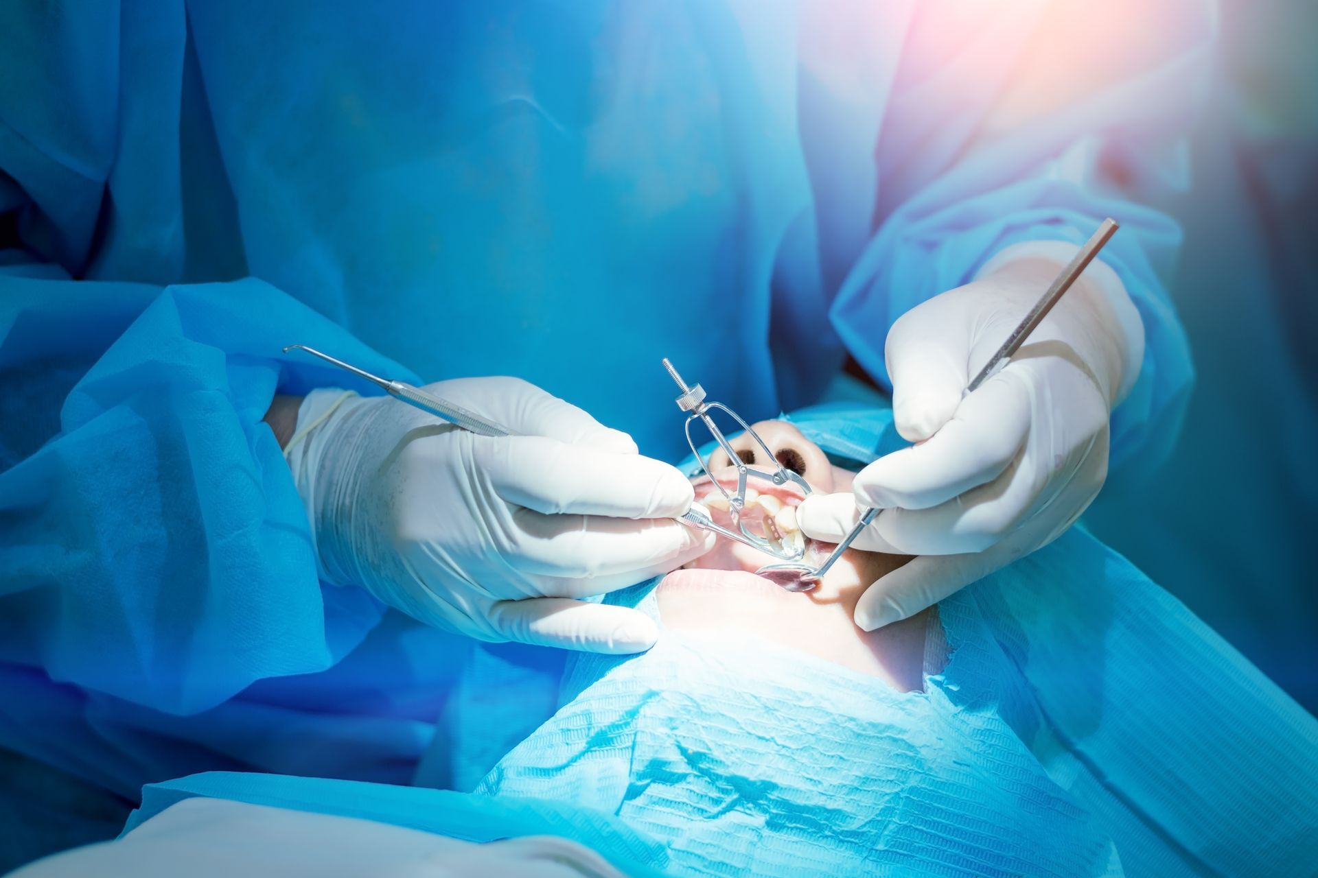 Surgeons’ gloved hands perform a procedure under bright light, with blue surgical drapes covering the patient.