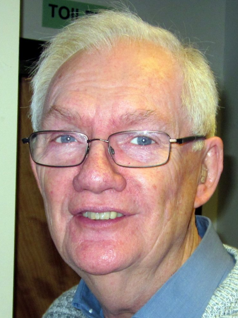 Man wearing glasses smiles, looking directly at the camera.