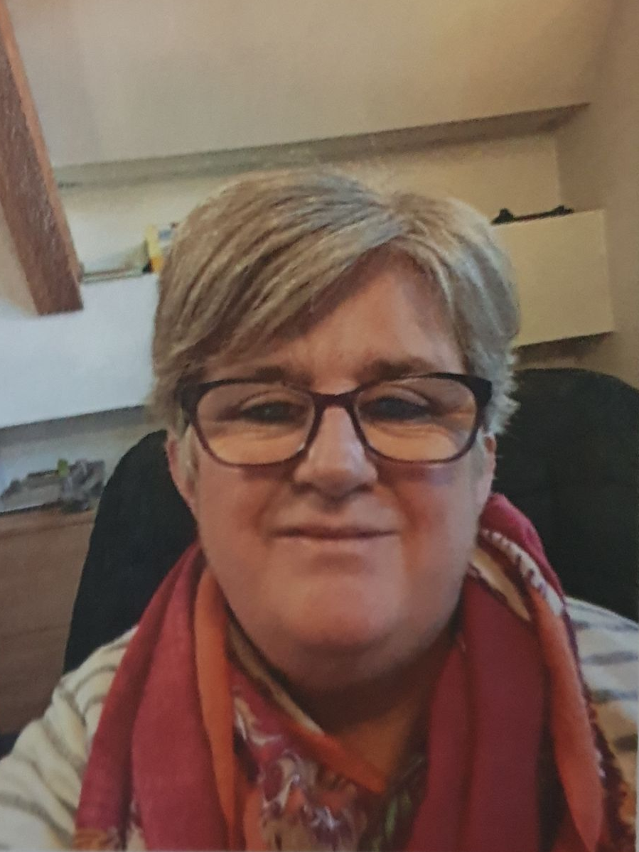 Woman with glasses smiles, wearing red scarf, in room with light-colored walls.