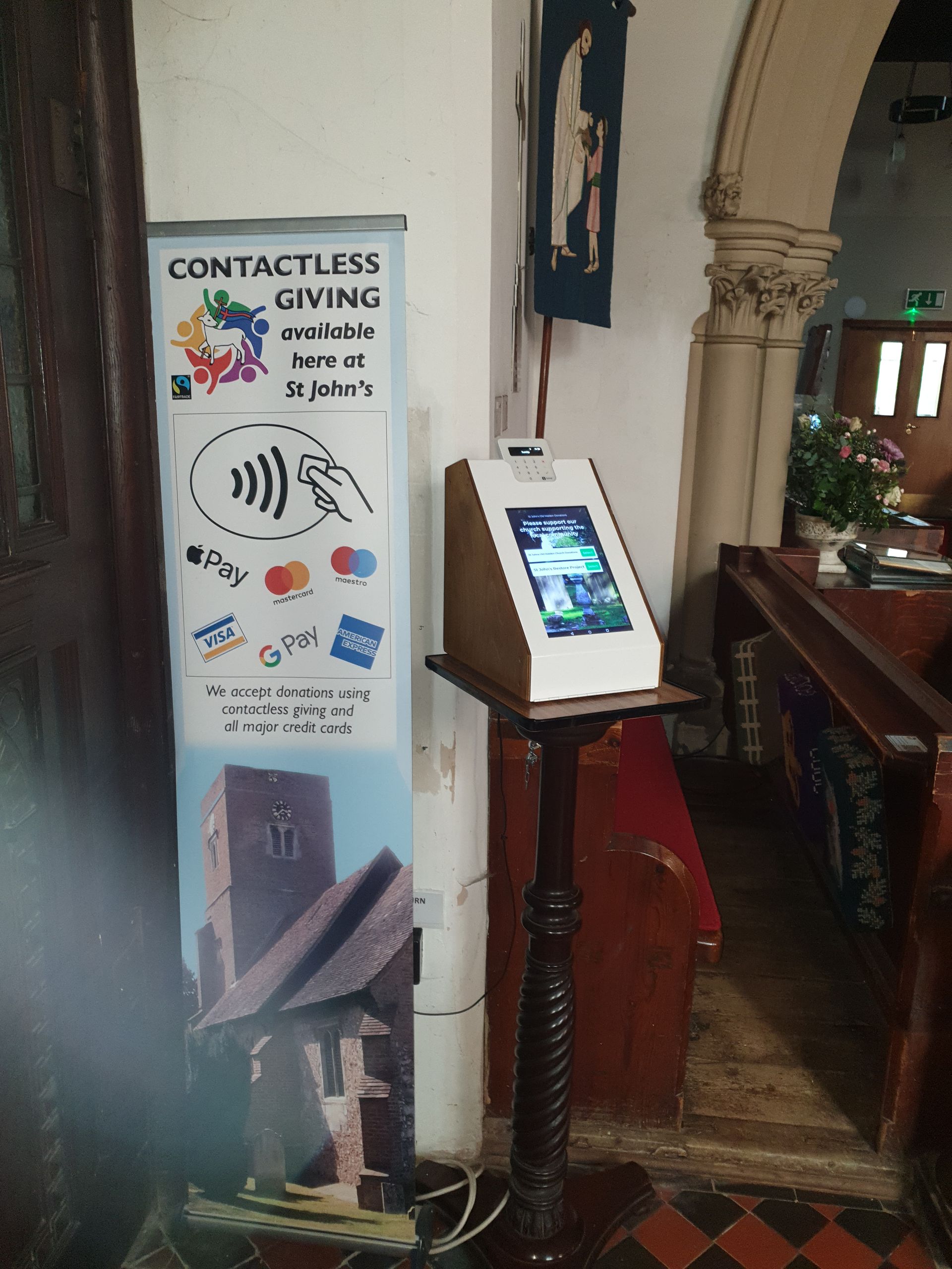 A contactless giving station in a church. Signage and a digital display on a stand.