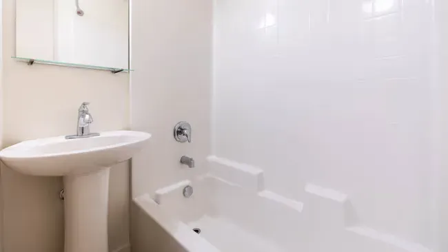 White bathroom with pedestal sink, bathtub, and mirror.