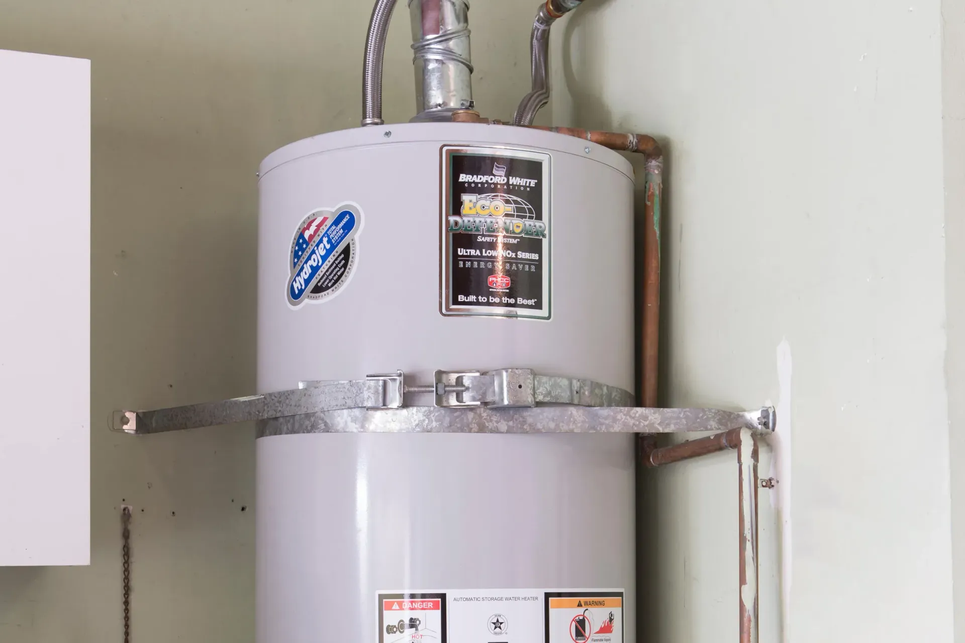 A white water heater is sitting on a wall in a room. A white water heater is sitting on a wall in a room.