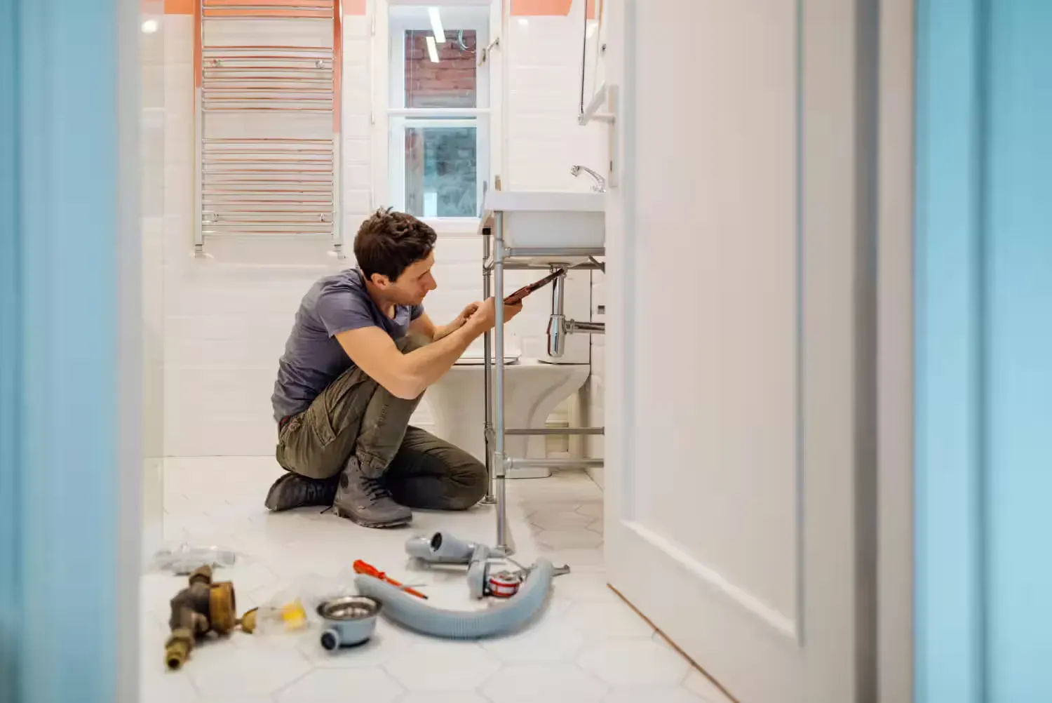 A man is kneeling on the floor fixing a sink in a bathroom.