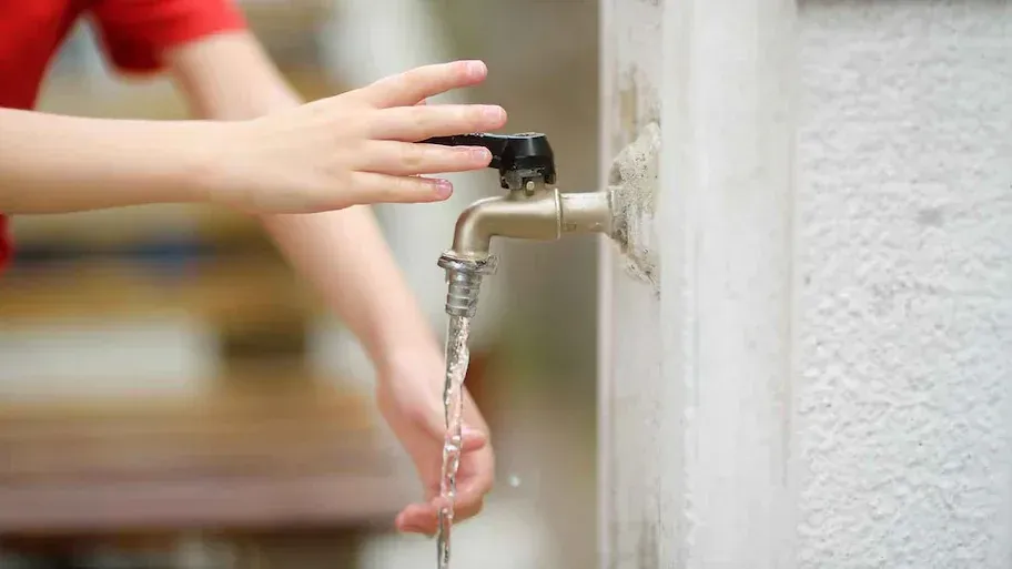 A child is washing their hands under a faucet.