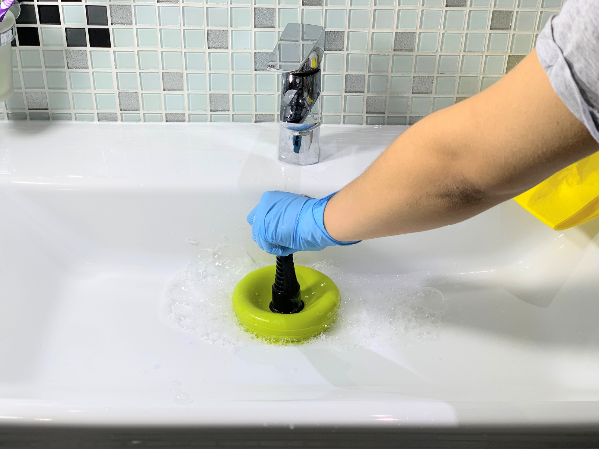 A person is using a plunger to clean a bathroom sink.