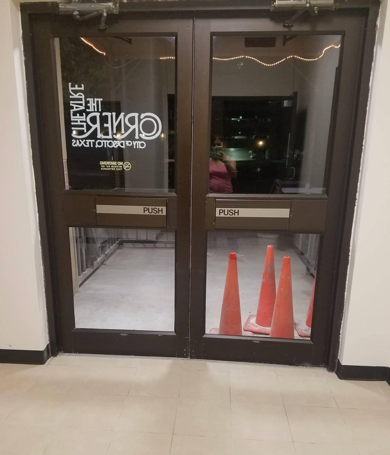 Double glass doors to The Theatre at Grand Prairie, with orange traffic cones visible inside through the glass.
