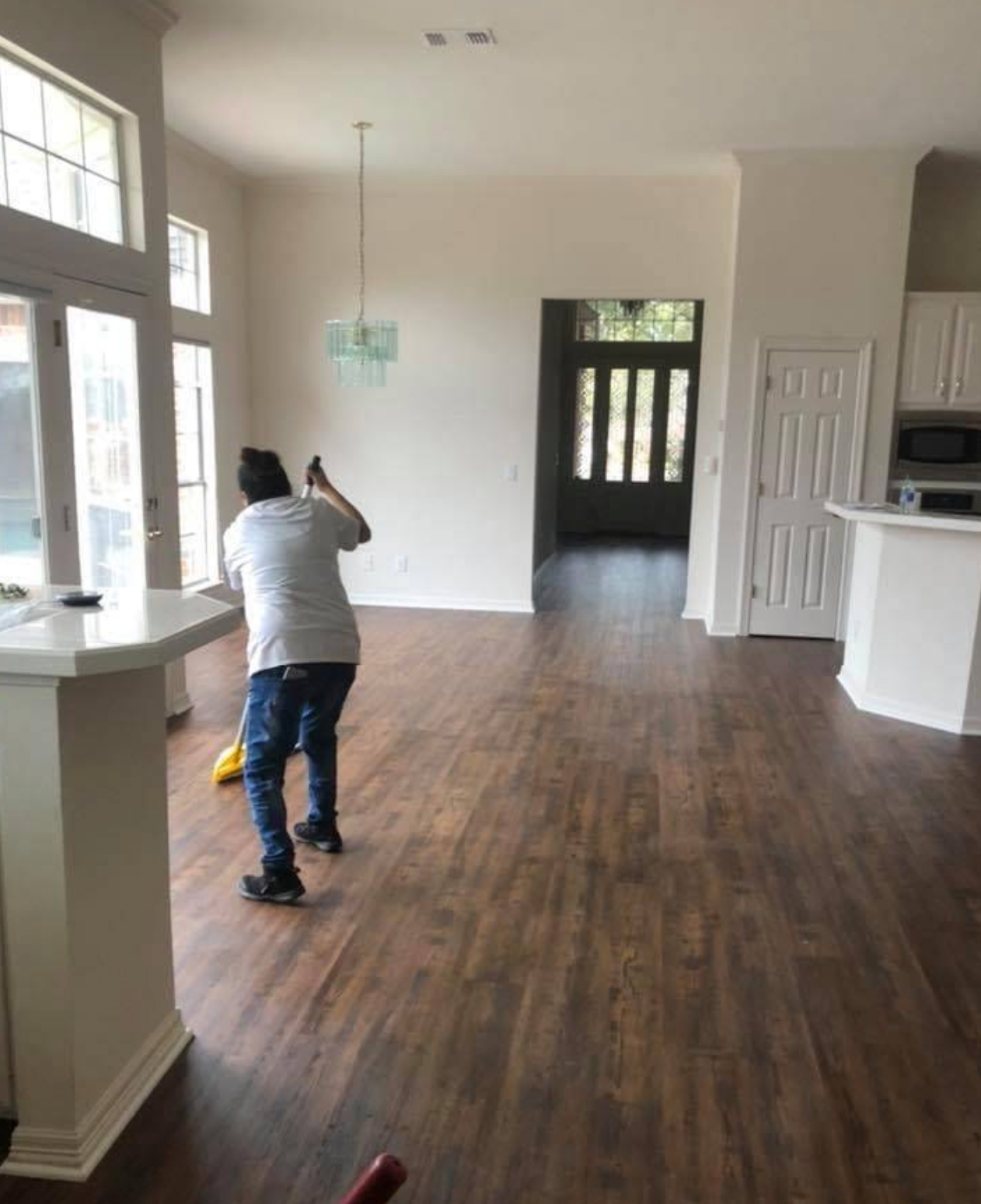 A person in a white shirt and jeans mops the dark wood floor of a bright, open-concept home interior.