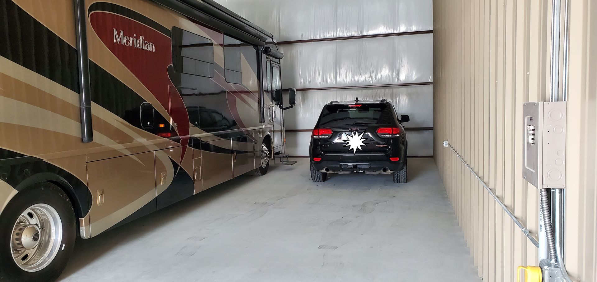 A rv and a car are parked in a garage.