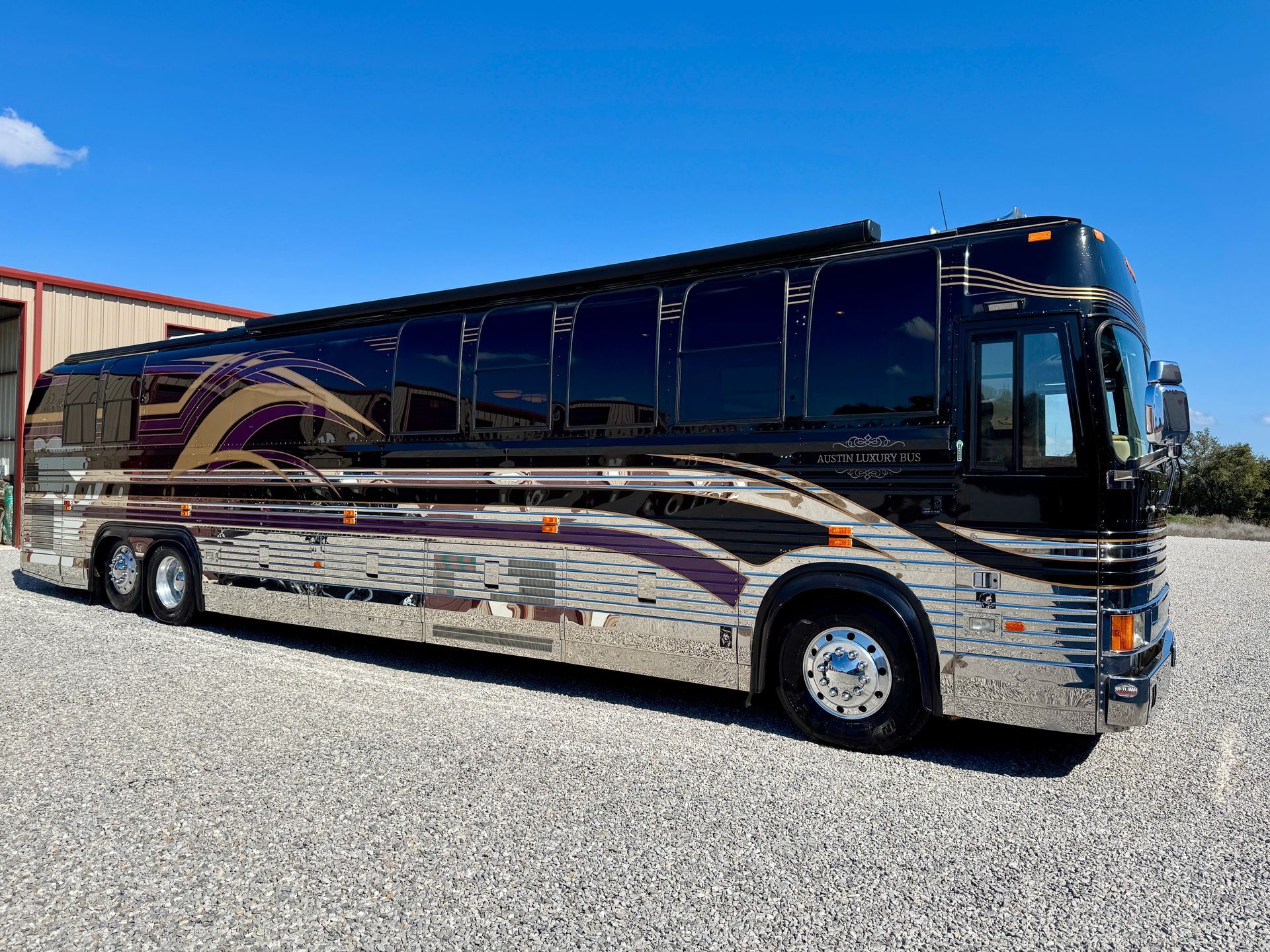 A large bus is parked in a gravel lot in front of a building.