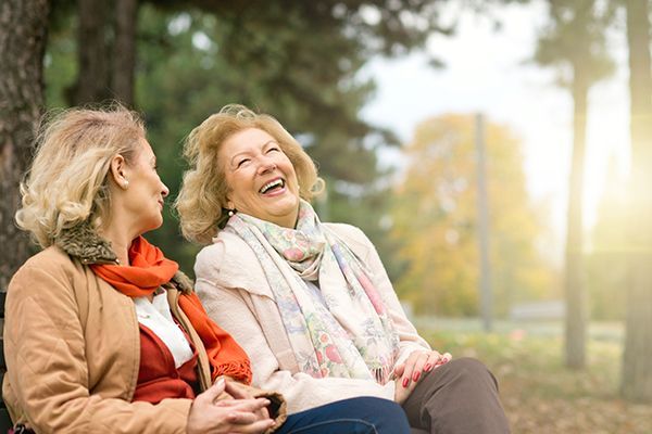 two older women are sitting on a park bench laughing .