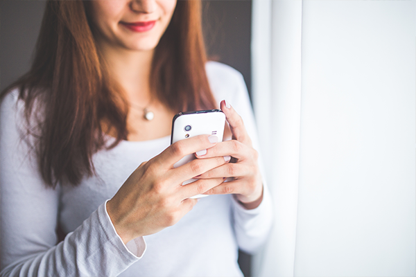 a woman is holding a cell phone in her hands in front of a window .