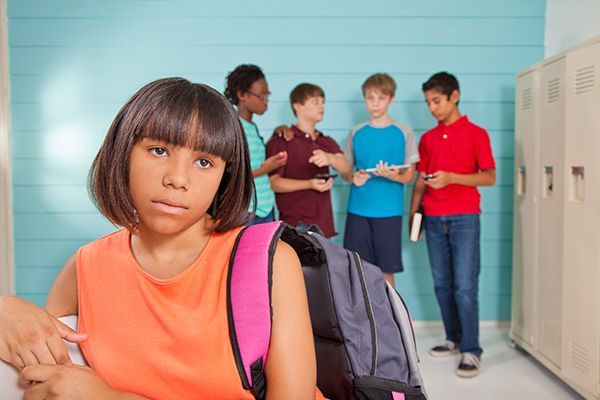 a girl with a backpack is sitting in a locker room with other students .