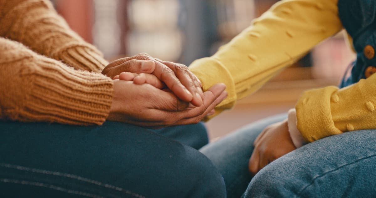 A woman and a child are holding hands while sitting on the floor.