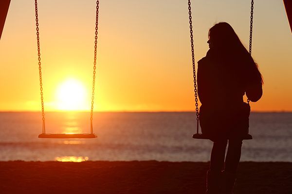 a woman is sitting on a swing on the beach at sunset .