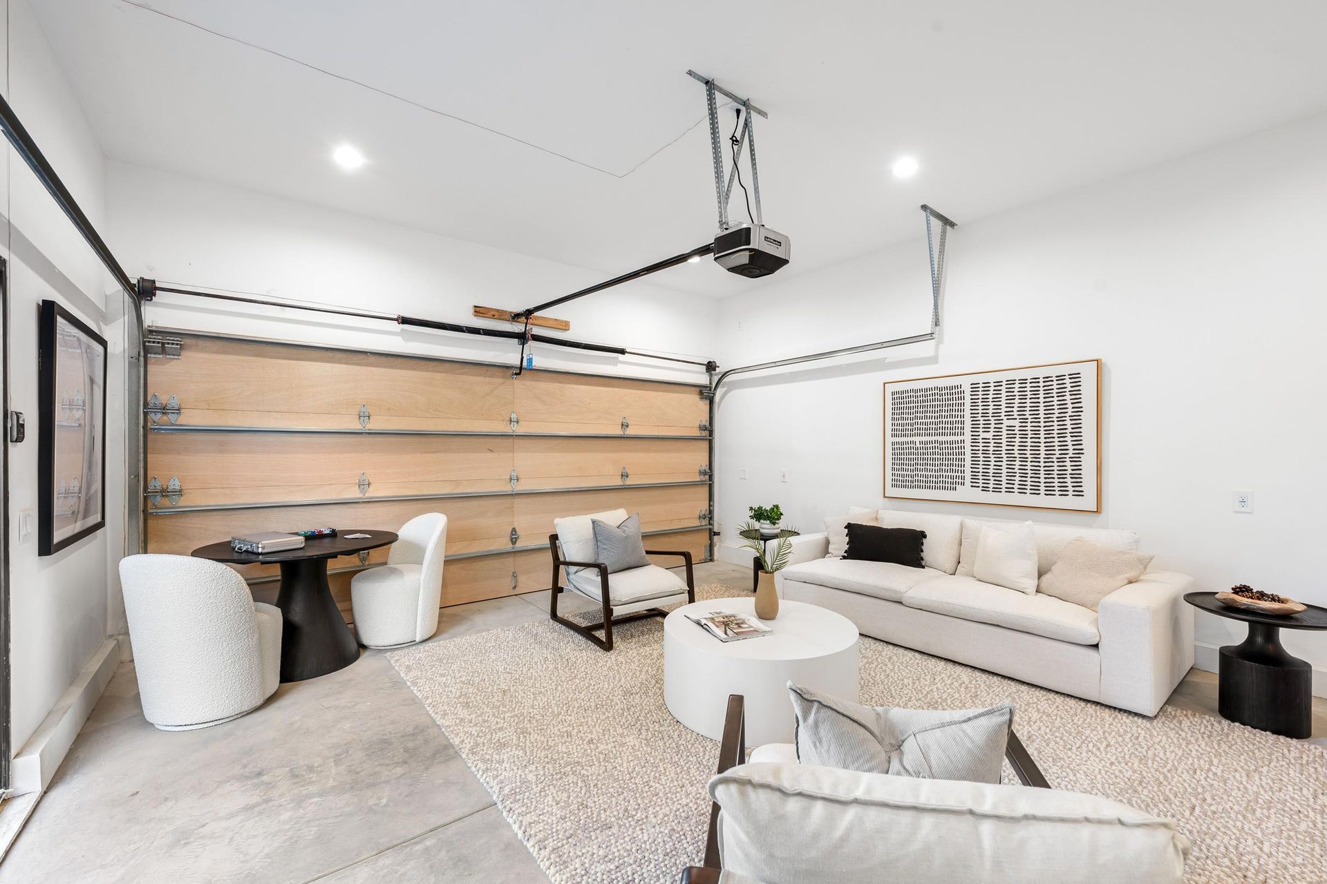 Modern living room with garage door, white furniture, rug.
