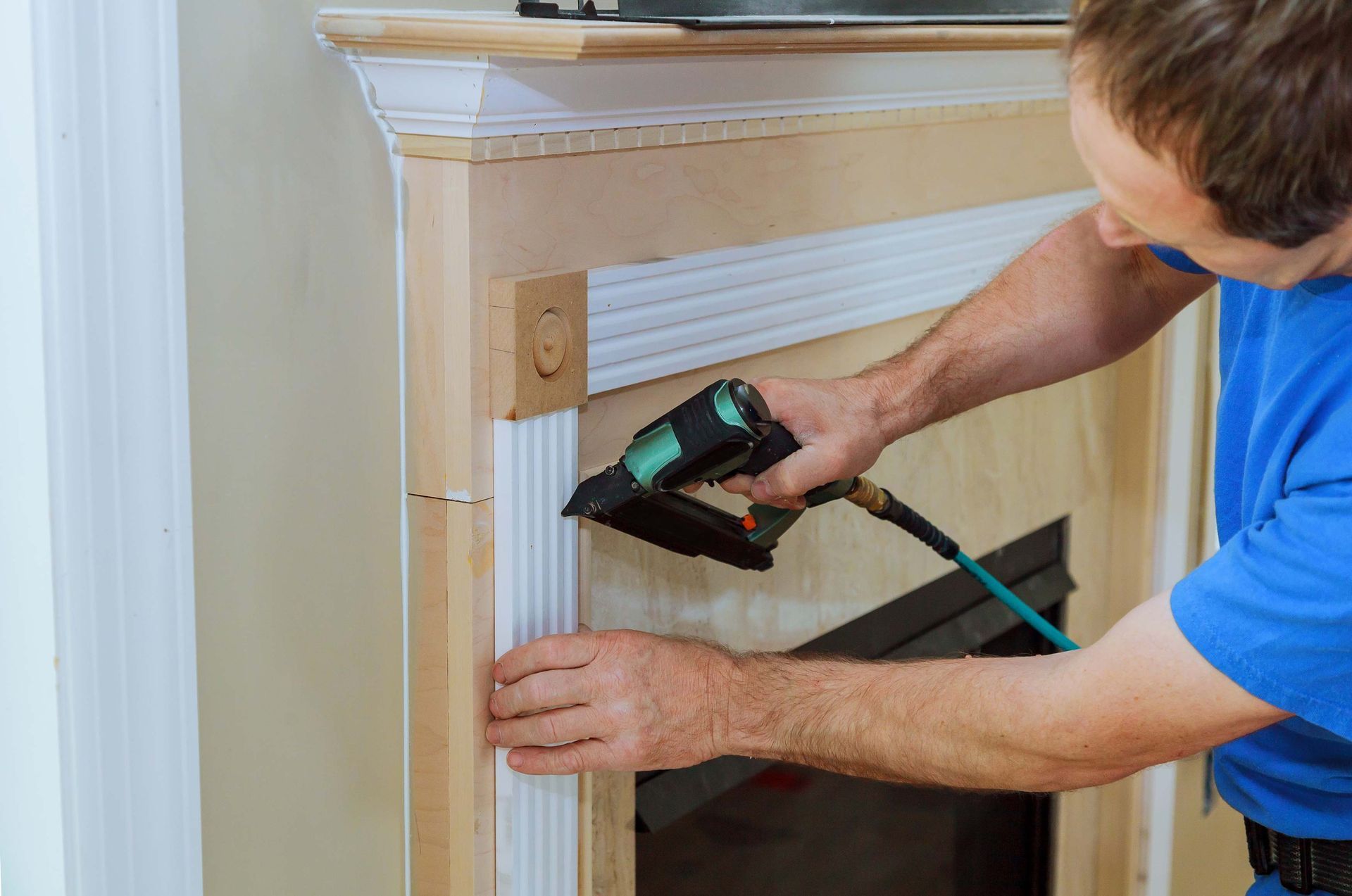 Man using a nail gun to attach trim around a fireplace.