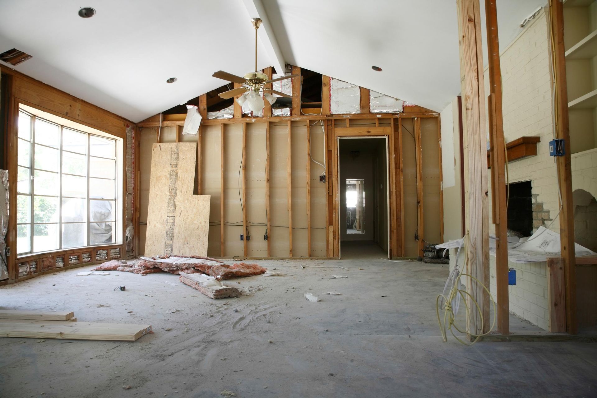 Room undergoing renovation: exposed framing, concrete floor, open doorway, window.