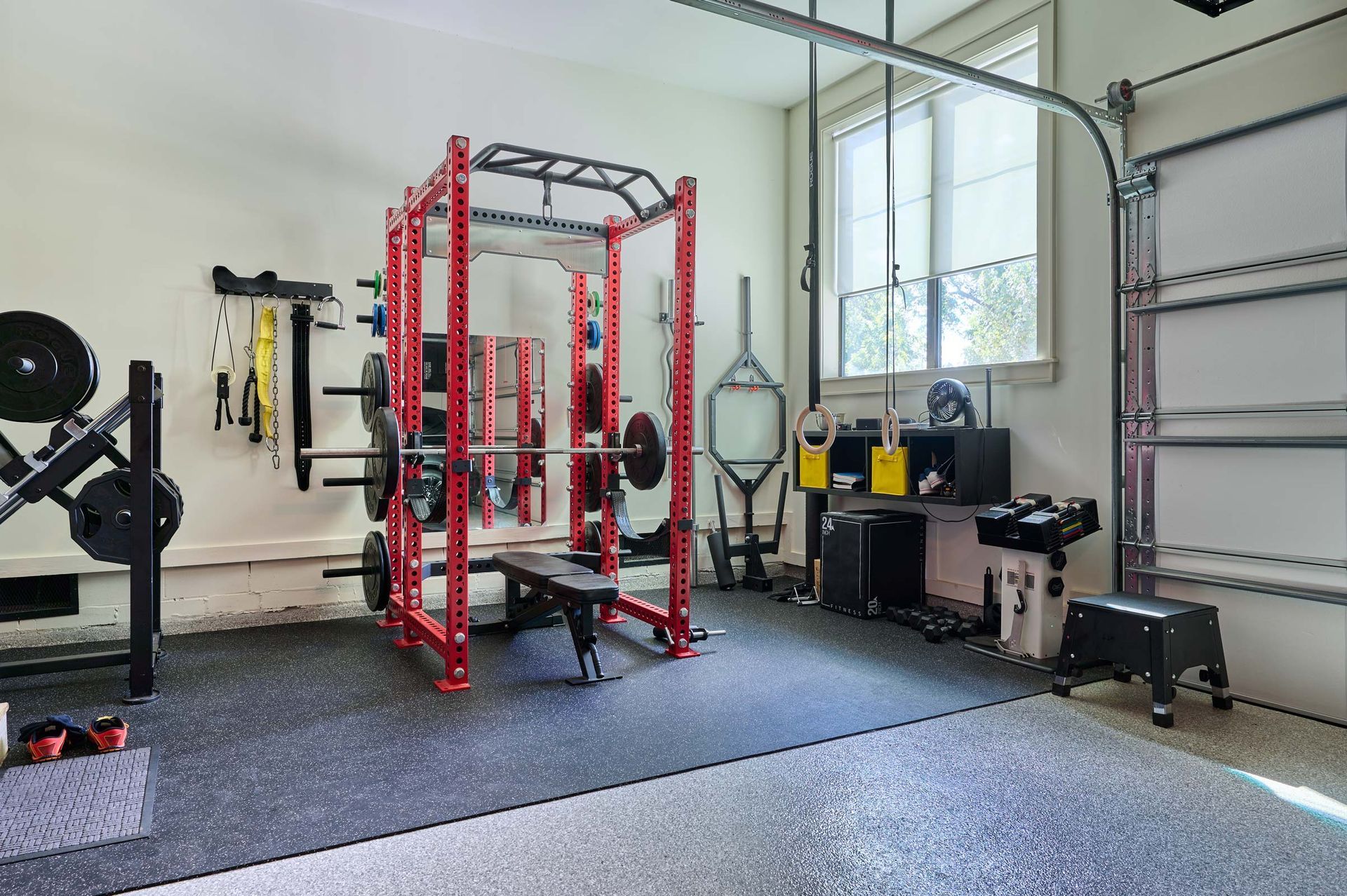 Home gym: red weight rack, bench, barbell, weights, and accessories on a rubber floor in a garage.