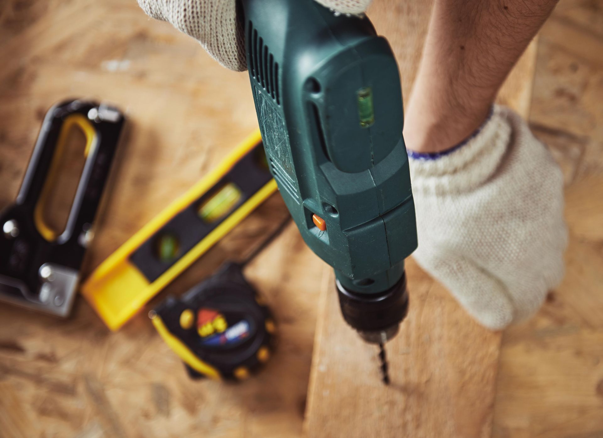 Person using a power drill on a wooden surface, with other tools nearby.