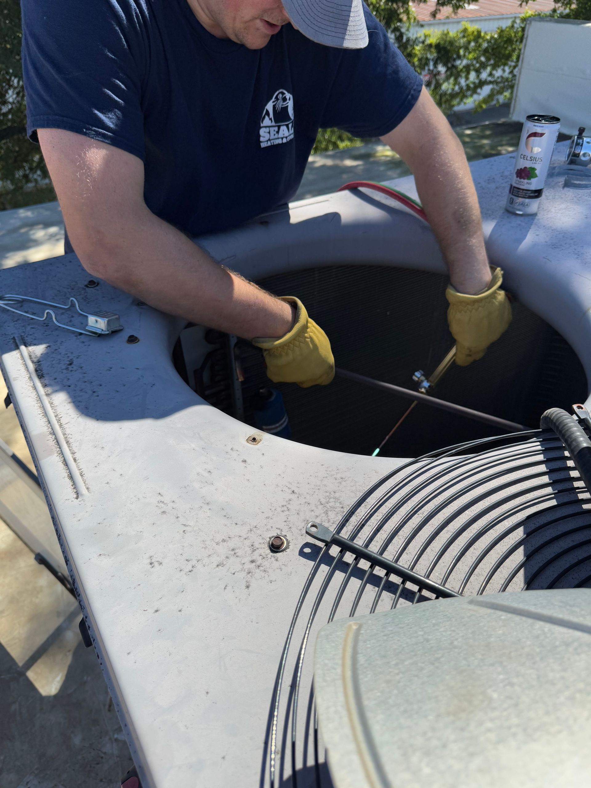 Man in gloves working on an air conditioning unit on a rooftop.