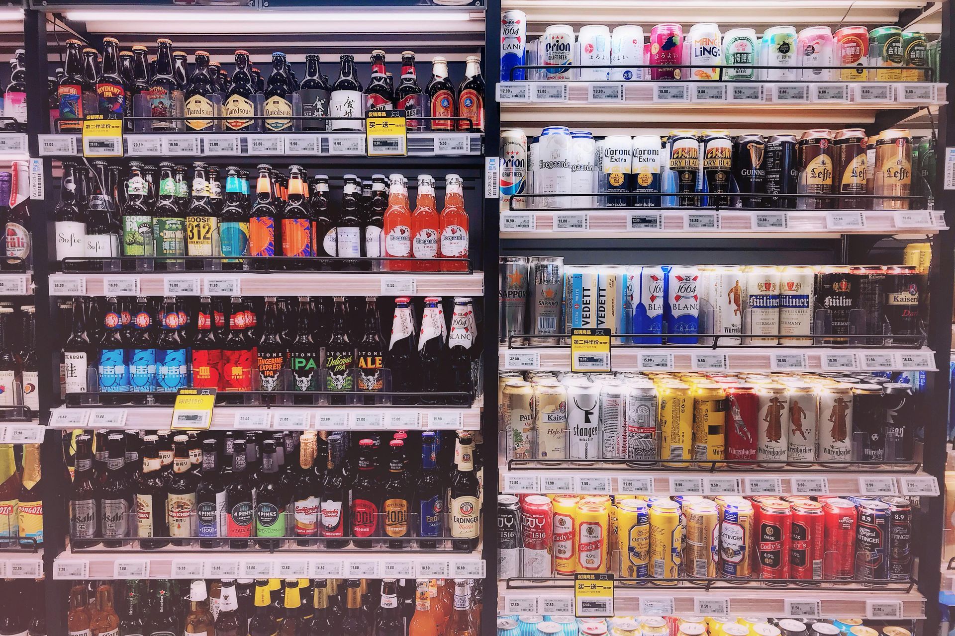 Shelves of beverages in a store. Bottles and cans of various drinks displayed under bright lights.