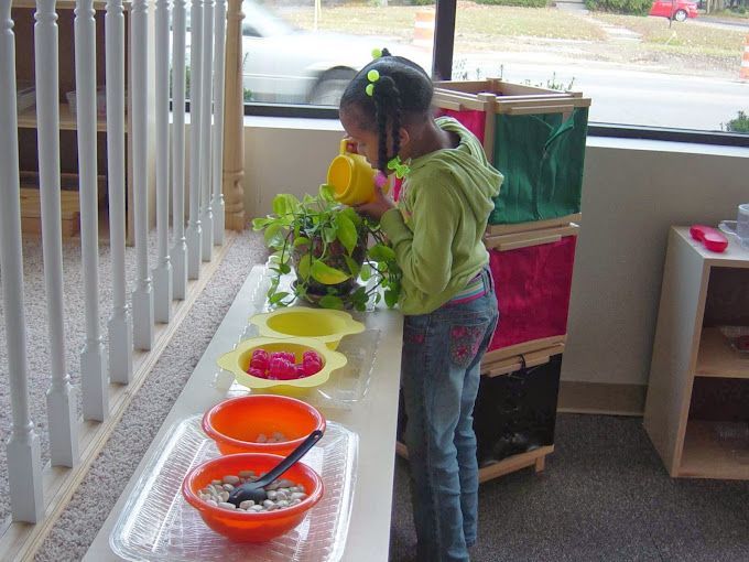 A little girl is watering a plant with a yellow watering can