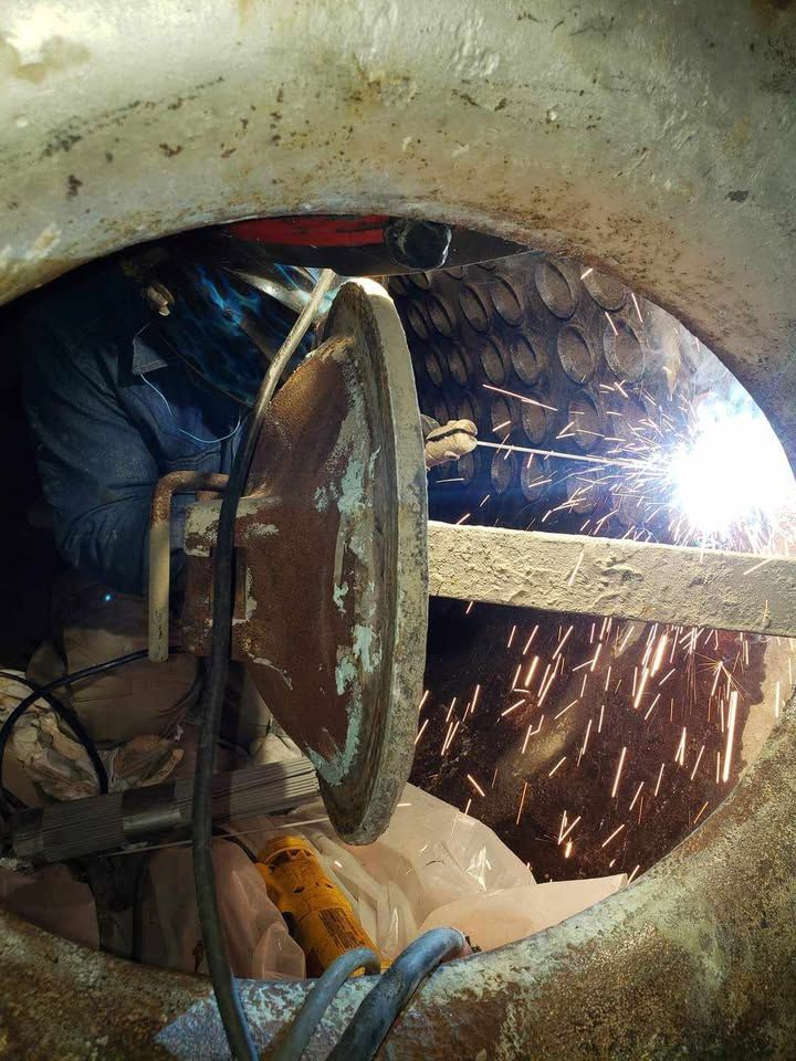 A man is welding a piece of metal in a hole.