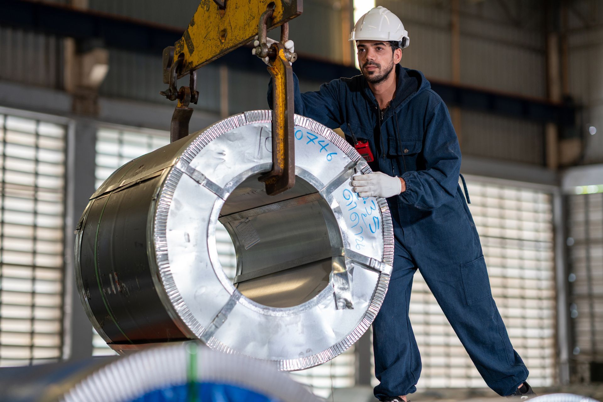 A man is lifting a large metal coil with a crane in a factory.
